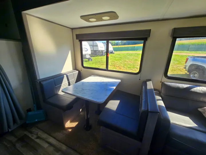 RV rental interior: A sunny dinette area with booth seating, a white marble-look table, and large windows showing campers outside.. Coleman Lantern LT 26BH 2022