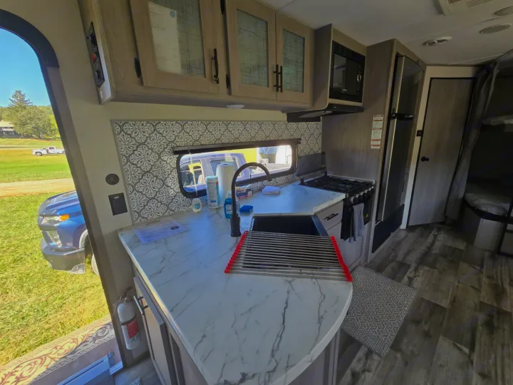 Modern RV rental kitchen with marble-look counter, black appliances, patterned backsplash, and window view.. Coleman Lantern LT 26BH 2022