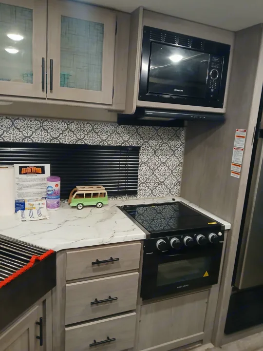This RV rental features a modern kitchen: light wood cabinets, marble counter, black appliances, and patterned backsplash.. Coleman Lantern LT 26BH 2022