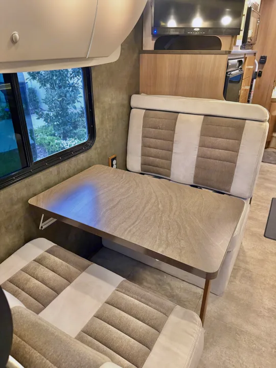 Modern rv rental interior featuring a cozy dinette with two-tone benches, light table, window, and TV/kitchenette.. Winnebago Trend 2015
