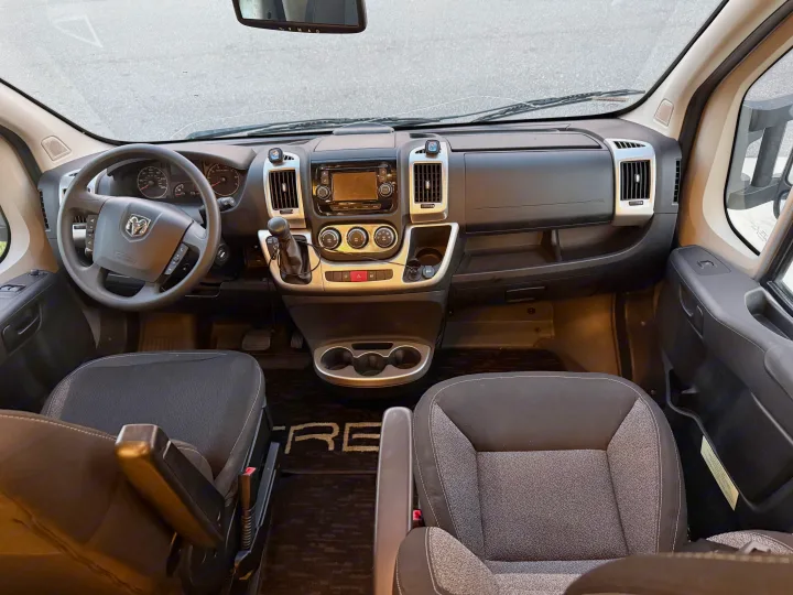 Inside your next RV rental. Front cabin view showing the dashboard, steering wheel, infotainment, climate controls, and seats.. Winnebago Trend 2015