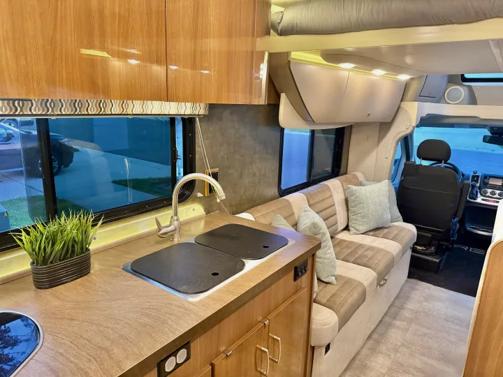 Cozy rv rental interior: compact kitchen with sink, sofa seating, and an overhead bed, optimizing small space living for travel.. Winnebago Trend 2015
