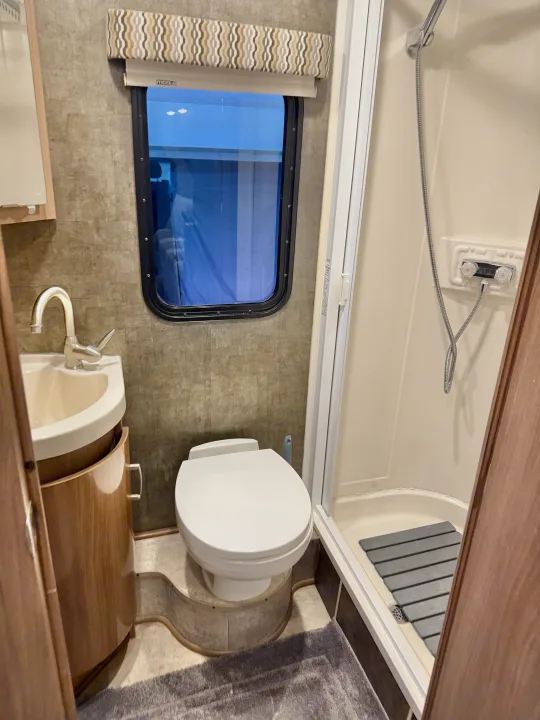 Compact RV rental bathroom showing a sink, toilet, and shower. Efficient design for travel.. Winnebago Trend 2015