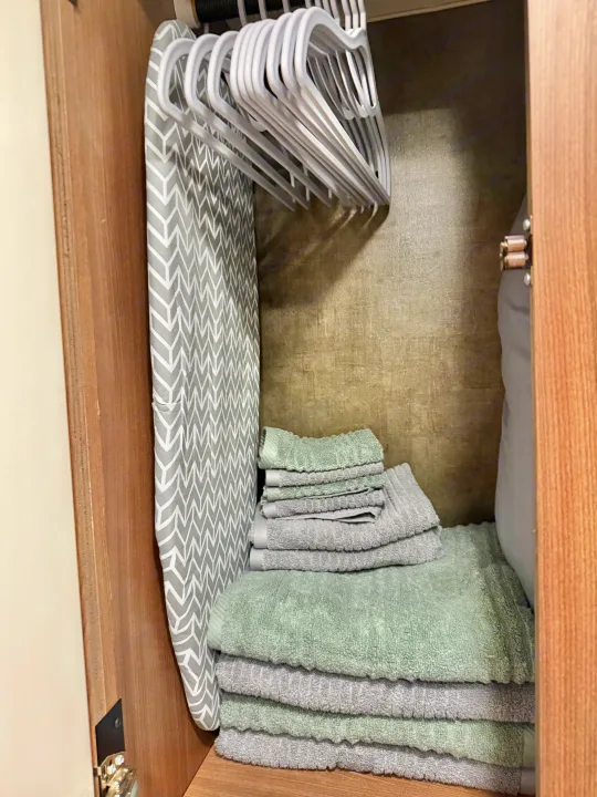 RV rental: Compact closet with an ironing board, white hangers, and stacks of fresh green & grey towels.. Winnebago Trend 2015