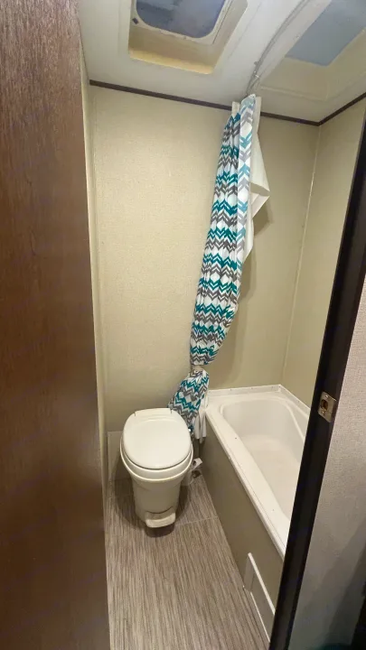 This RV rental features a compact bathroom with a white toilet, small tub/shower, and a teal/grey patterned curtain.. Primetime Avenger 2019