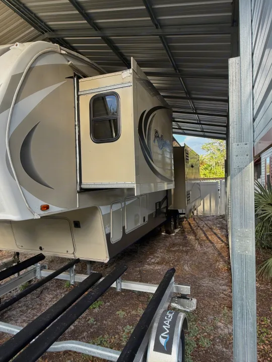 Spacious Reflection RV rental under a metal carport, with a boat trailer visible below.. Grand Design Reflection 2015