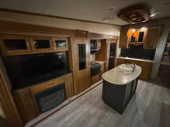 This RV rental interior features a full kitchen with an island, stove, microwave, and a living area with a TV and fireplace.. Grand Design Reflection 2015