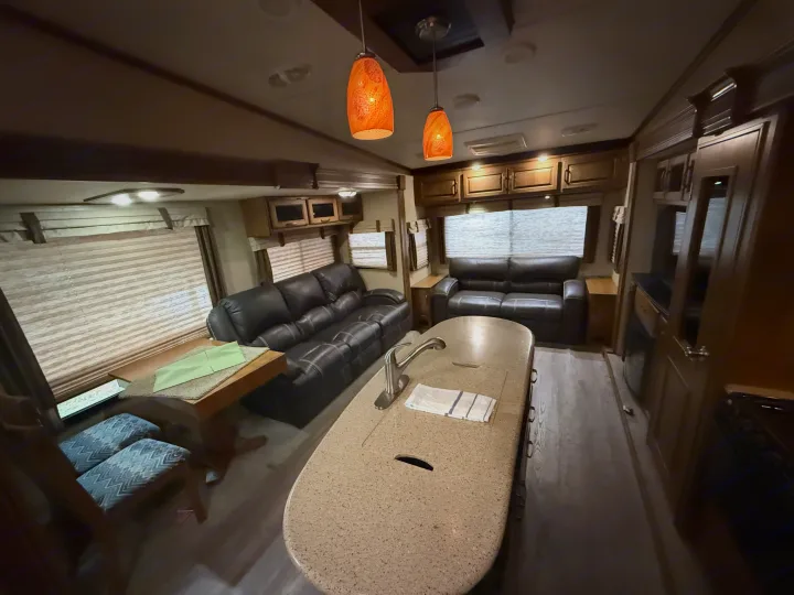 Cozy RV rental interior: black leather couches, kitchen island with sink, dining table & chairs. Well-lit living space.. Grand Design Reflection 2015