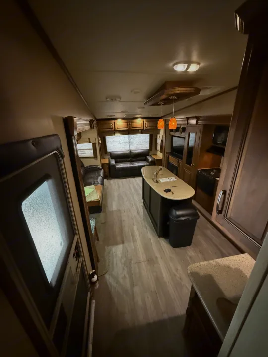 Interior view of an RV rental, showing a modern living room with a black couch, kitchen island, and light wood floors under warm lighting.. Grand Design Reflection 2015