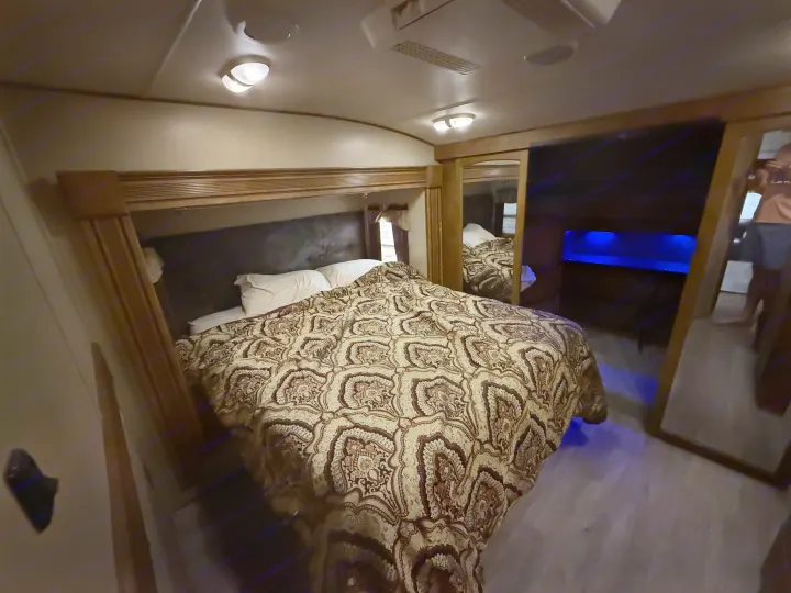 Cozy RV rental bedroom with a large bed, patterned comforter, and mirrors, illuminated by ambient blue light.. Grand Design Reflection 2015
