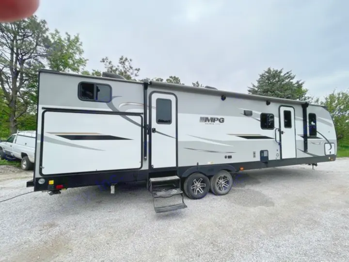 Modern gray and white travel trailer RV rental with an extended slide-out and steps down, parked on a gravel lot.. Cruiser RV MPG Ultra Lite 2021