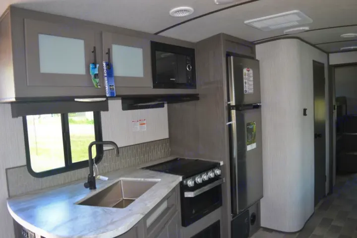 Modern RV rental kitchen with stainless steel appliances, sink, light countertop, and grey cabinets.. Cruiser RV MPG Ultra Lite 2021