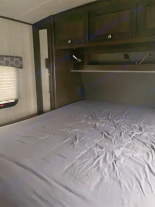 Cozy RV rental bedroom showcasing dark cabinets, a reading light, and a bed with rumpled grey sheets.. Cruiser RV Shadow Cruiser 2020