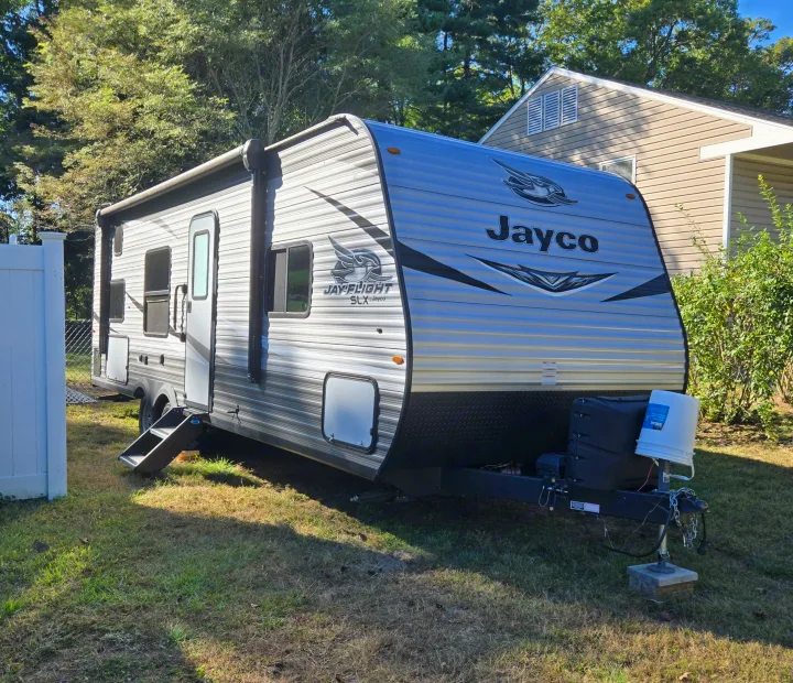 A Jayco Jay Flight SLX travel trailer (RV rental) is parked on a grassy lawn next to a house under a clear sky.. Jayco Jay Flight SLX 2021