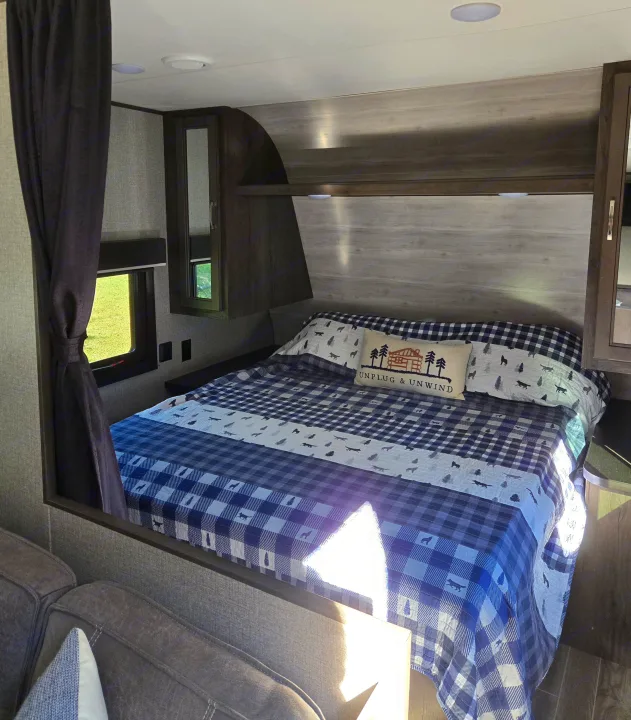 Comfortable RV rental bedroom with blue plaid bedding, "UNPLUG & UNWIND" pillow, and a window for scenic views.. Jayco Jay Flight SLX 2021