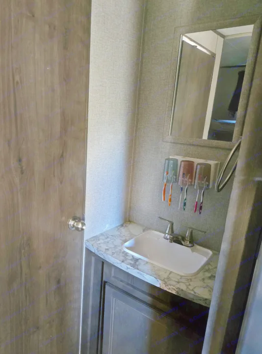 RV rental bathroom with sink, mirror, toothbrushes, and a dark wooden door. Textured walls and marble-patterned counter.. Jayco Jay Flight SLX 2021
