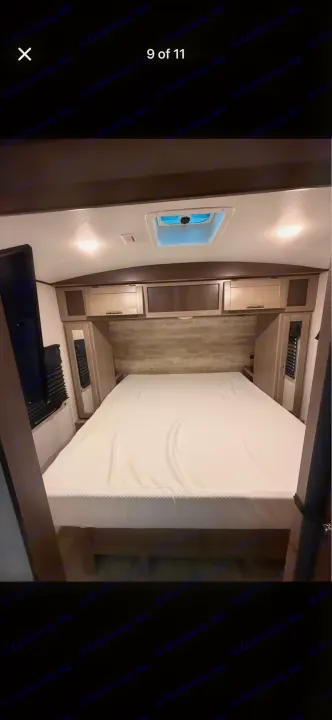 Clean and cozy RV rental bedroom featuring a comfortable bed, overhead storage, and a mounted TV.. Crossroads RV Sunset Trail Super Lite 2021