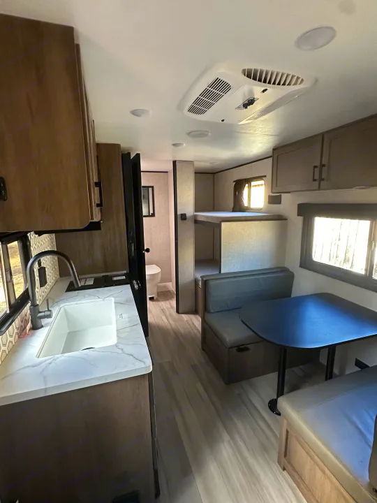 Modern RV rental interior: kitchen with sink, dinette, and bunk beds. Efficient layout for travel comfort.. Starcraft Autumn Ridge 2025