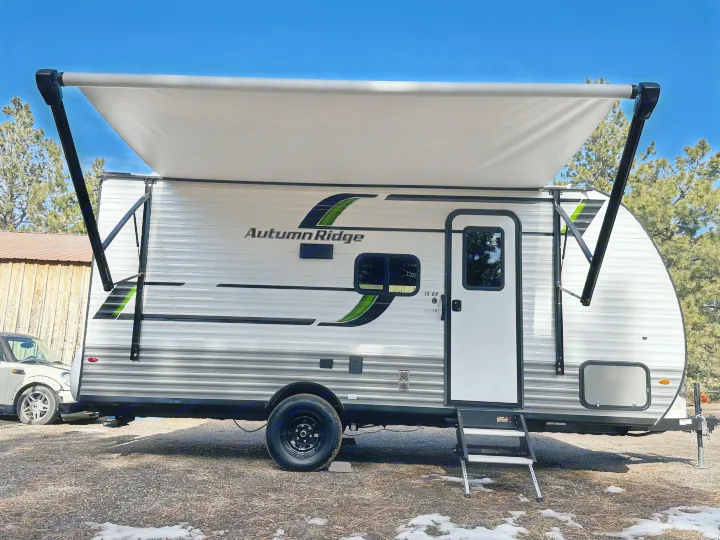 White & gray Autumn Ridge travel trailer (camper) rv rental with extended awning, visible steps, and a single wheel.. Starcraft Autumn Ridge 2025