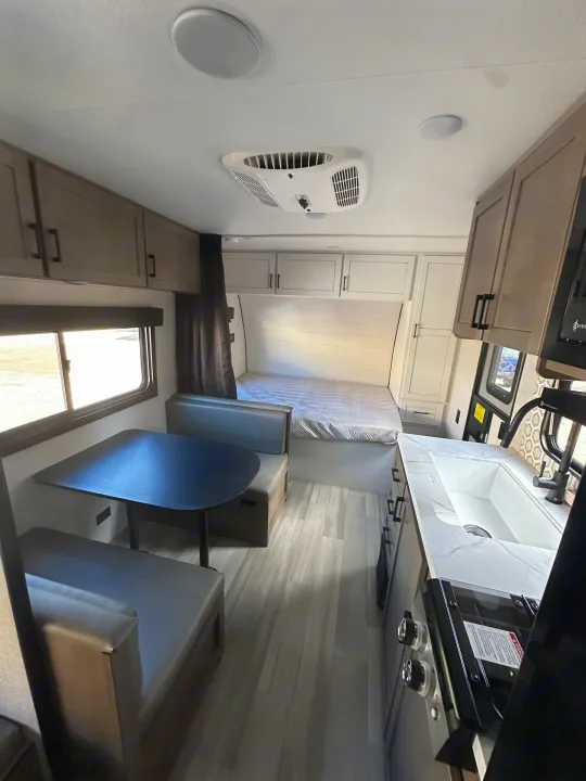 RV rental: A bright, modern interior featuring a kitchenette with a white sink, dining booth, and a bed in the background.. Starcraft Autumn Ridge 2025