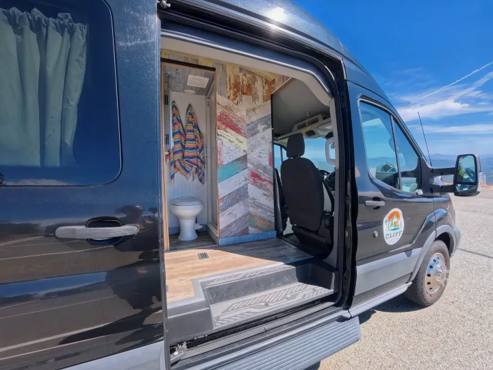 Black camper van RV rental with open door, showcasing a custom interior featuring a built-in toilet and colorful decor.. Ford Transit Custom 2015