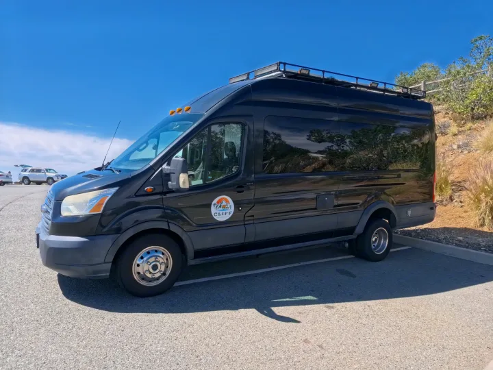 Black custom camper van RV rental from CLIFF. Equipped with a roof rack and lights, ready for adventure travel.. Ford Transit Custom 2015