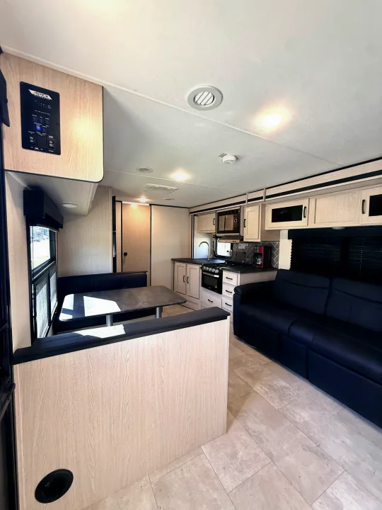 RV rental interior: cozy dinette, modern kitchen, and comfortable sofa with light wood cabinetry and tile-look flooring.. Coachmen Apex 2022