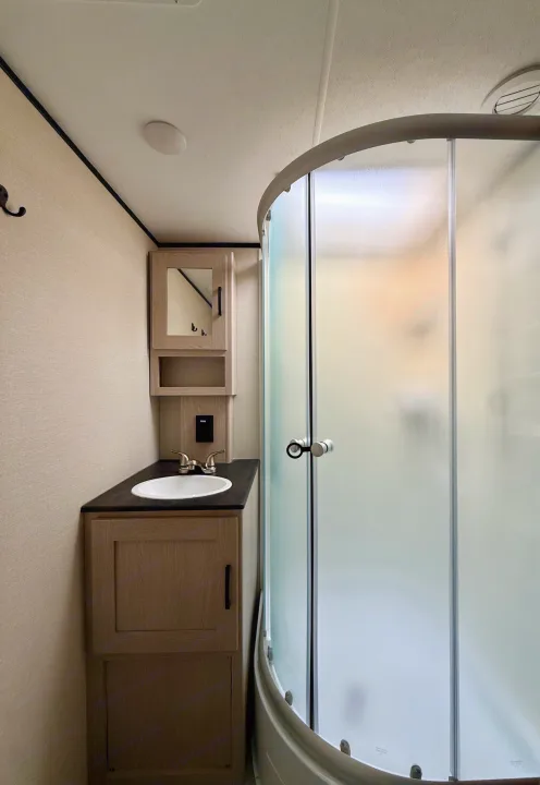 Modern RV rental bathroom features a sink, wood vanity, mirrored cabinet, and space-saving frosted glass shower.. Coachmen Apex 2022