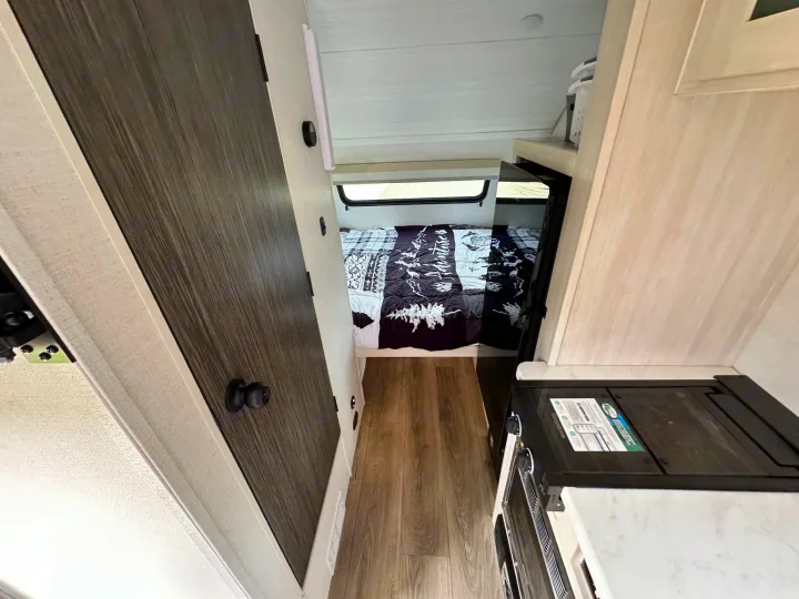 RV rental interior featuring a hallway leading to a cozy bedroom with a window, and a compact kitchenette on the right.. Forest River RPod 2026