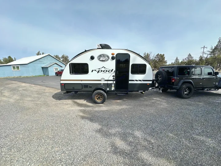 A modern white and grey r.pod teardrop RV rental is hitched to a dark grey Jeep, ready for off-road camping adventures.. Forest River RPod 2026