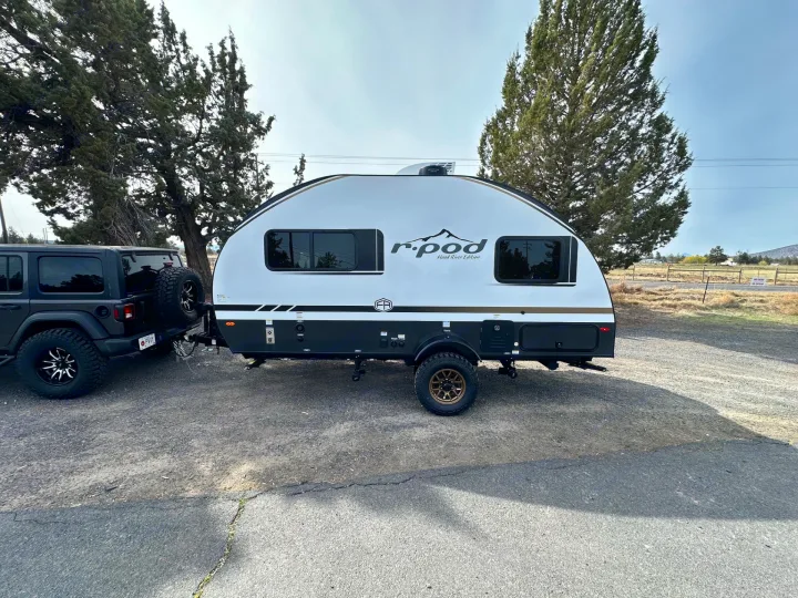 Black Jeep Wrangler towing a white r-pod Hood River Edition travel trailer. Perfect for your next rv rental camping adventure!. Forest River RPod 2026