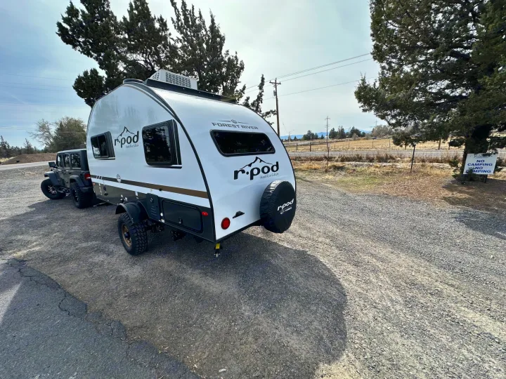 Forest River R-Pod Hood River Edition RV rental hitched to a Jeep Wrangler, parked on a gravel lot, ready for adventure.. Forest River RPod 2026