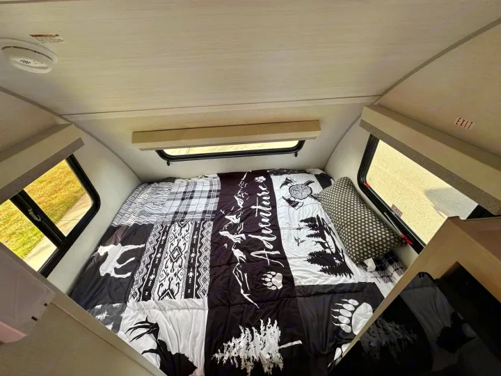 Cozy RV rental sleeping area with an adventure-themed bed, windows, and a smoke detector on the ceiling.. Forest River RPod 2026