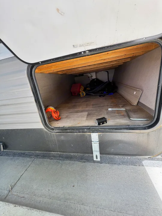 Open RV rental pass-through storage compartment with camping equipment, tools, and a gas can inside.. Coleman Cch 2022