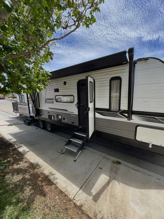 This Coleman rv rental features an open door, extended awning, and steps, parked roadside on a bright day.. Coleman Cch 2022