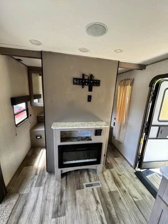 RV rental living space with a modern fireplace, wall-mounted TV bracket, and wood-look flooring. Clean and functional interior.. Coleman Cch 2022