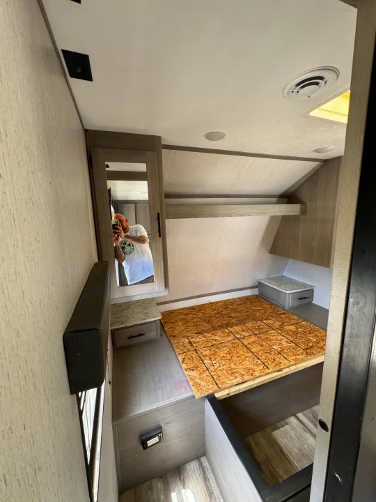RV rental bedroom: OSB bed platform, nightstands, and overhead storage are visible. A person is reflected in the mirror.. Coleman Cch 2022