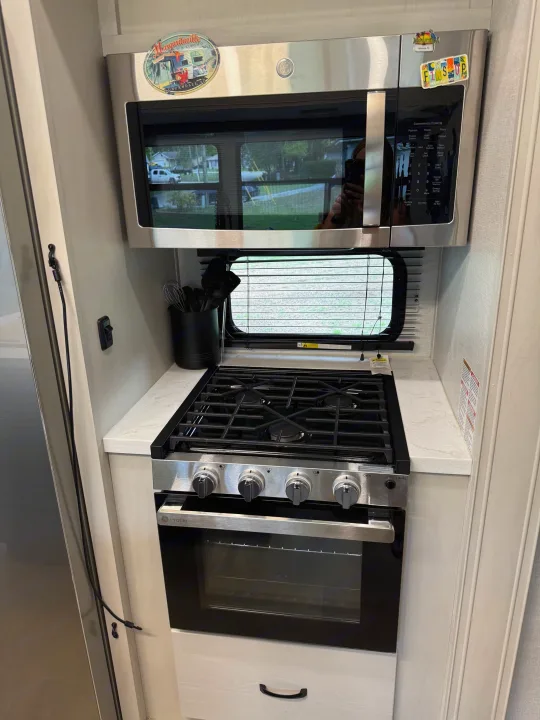 Modern RV rental kitchen featuring a stainless GE microwave, Profile gas range/oven, counter, and window with blinds.. Forest River Coachman Chaparral 2025