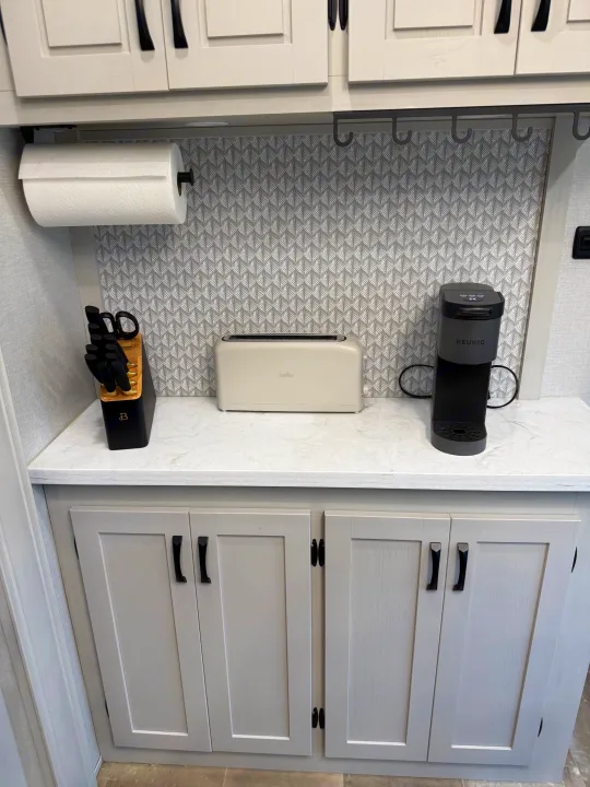 RV rental kitchen: A modern counter with a toaster, Keurig, and knife set. Features a patterned backsplash and light cabinets.. Forest River Coachman Chaparral 2025