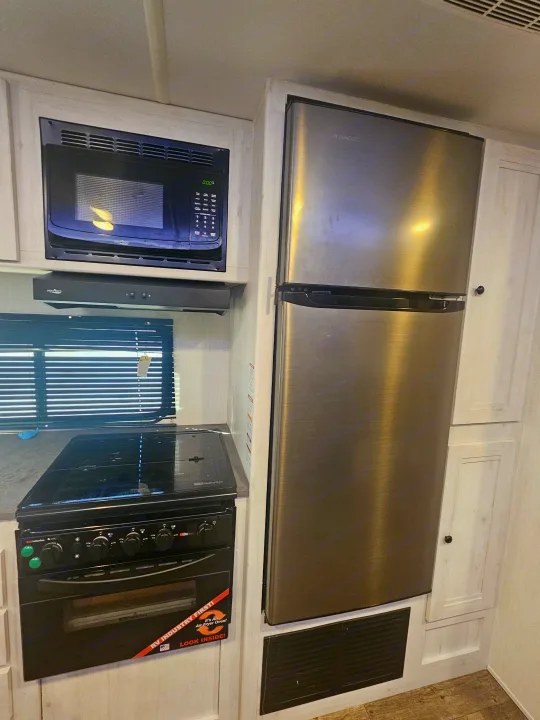 RV rental kitchen with a microwave, range hood, stainless steel refrigerator, and a Suburban stove with an air fryer oven.. Heartland RVs Trail Runner 2024
