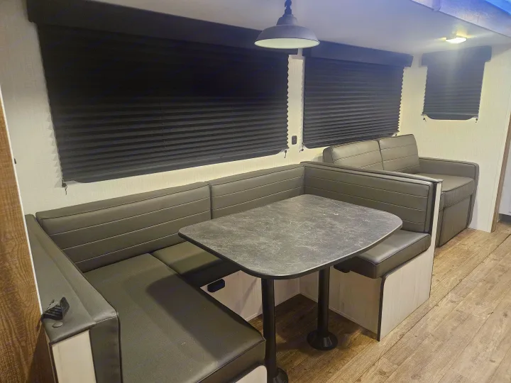 Interior view of an RV rental dinette, showcasing dark booth seating, a marbled table, and blackout blinds.. Heartland RVs Trail Runner 2024