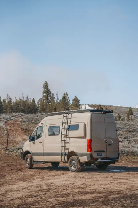 Adventure awaits! Tan Mercedes Sprinter rv rental on a dirt road, amidst trees & snow-dusted hills. Perfect outdoor travel.. Custom Mercedes Benz Sprinter 2022