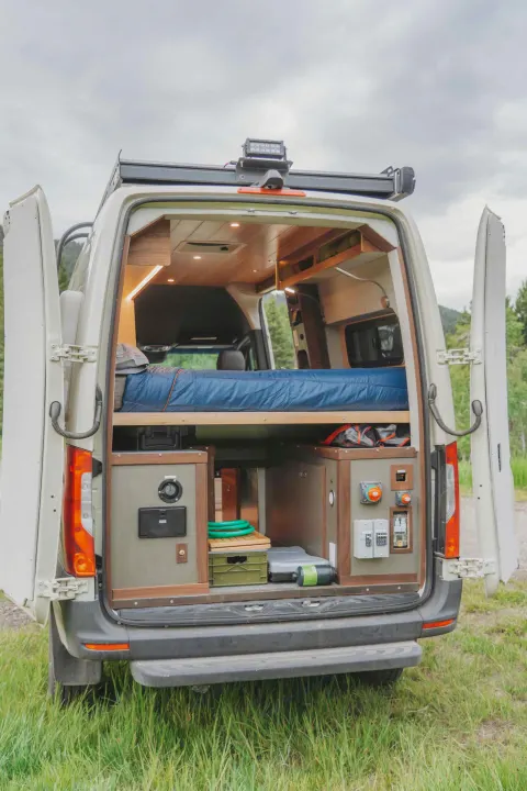 Explore this cozy RV rental's clever camper van interior, featuring a raised bed, organized storage, and utility panels for adventure.. Custom Mercedes Benz Sprinter 2022