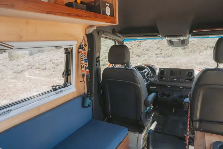 Experience an rv rental! View from the back into the driver's area, showing custom wood interior, window, and blue bench.. Custom Mercedes Benz Sprinter 2022