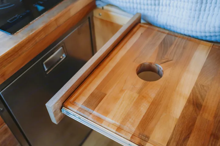 Space-saving pull-out wooden cutting board with a circular hole, perfect for food prep in this RV rental kitchen.. Custom Mercedes Benz Sprinter 2022
