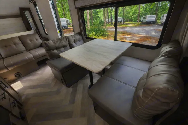 Inside this rv rental: dining table, comfy benches & sofa, large window with views of a wooded campground and other RVs.. Forest River Salem Cruise Lite 2020