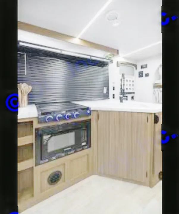 Modern RV rental kitchen with a compact design featuring a stovetop, built-in microwave, and light wood cabinetry.. Forest River Wildwood X-Lite 2025