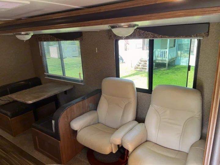 RV rental interior showcasing a cozy dinette with bench seats, two recliners, and bright windows with outdoor views.. Gulf Stream Conquest 2017