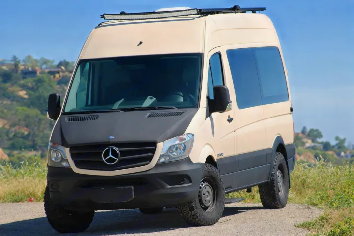 Adventure-ready Mercedes Sprinter RV rental, a beige van with off-road tires & roof light bar, parked outdoors.. Mercedes-Benz Sprinter 2008