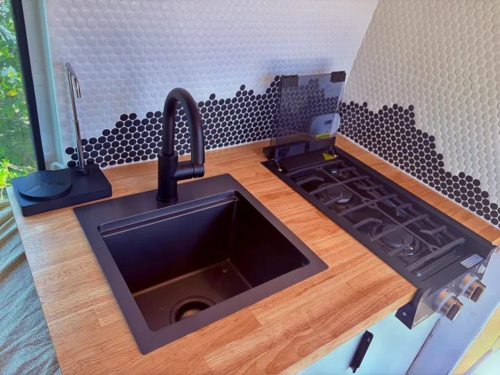 This RV rental features a modern kitchenette with a black sink, faucet, gas stove, wood counter, and unique penny tile backsplash.. Mercedes-Benz Sprinter 2008